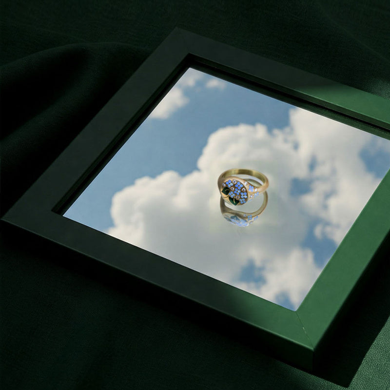 Gold ring with blue gemstone on a reflective surface, framed by a green border.