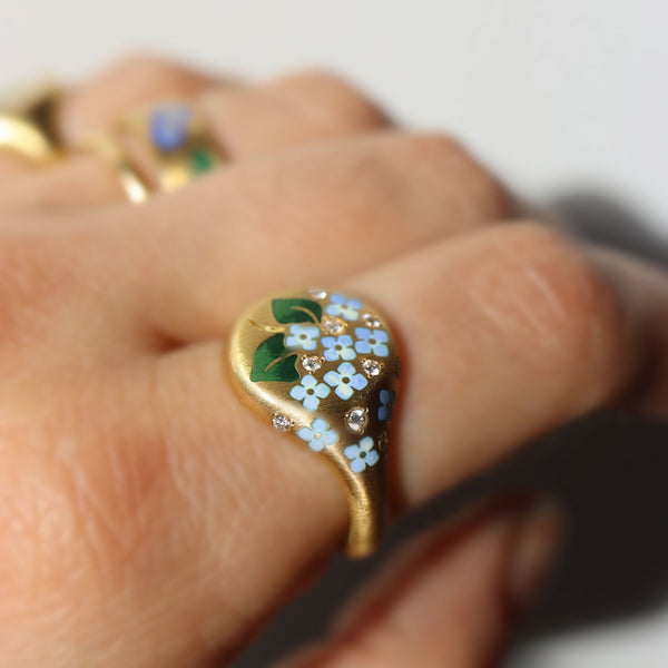 Gold ring with floral design on a finger against a neutral background