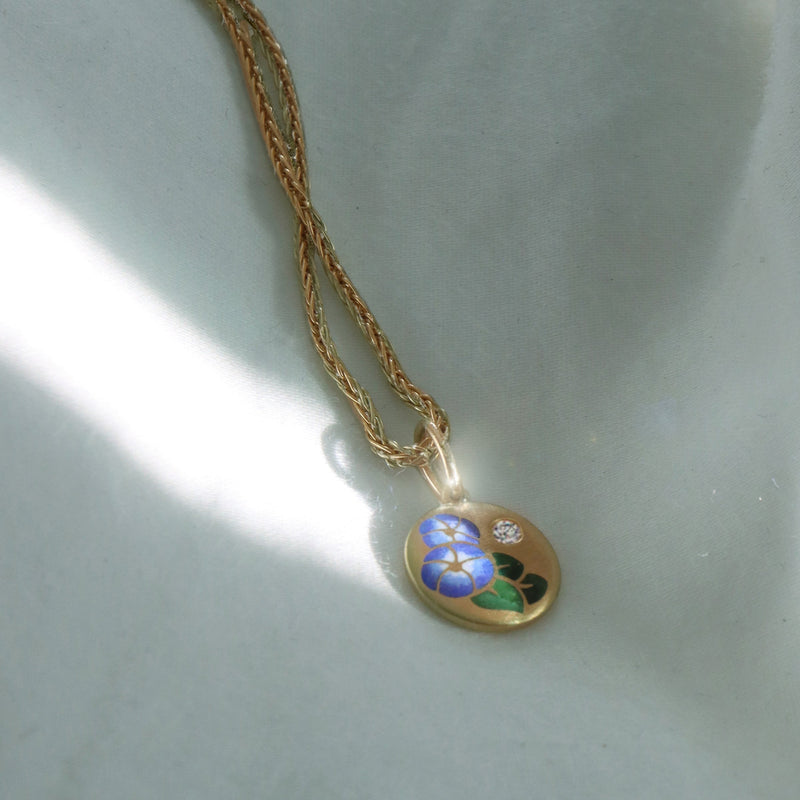 Gold enamel necklace with a pendant featuring a floral design on a light gray background