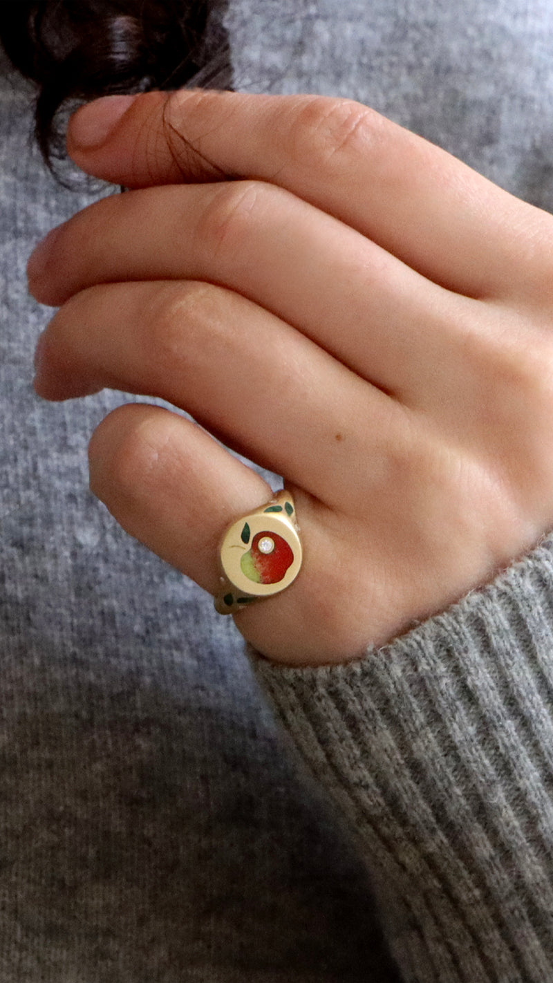 red enamel apple signet ring on a pink finger