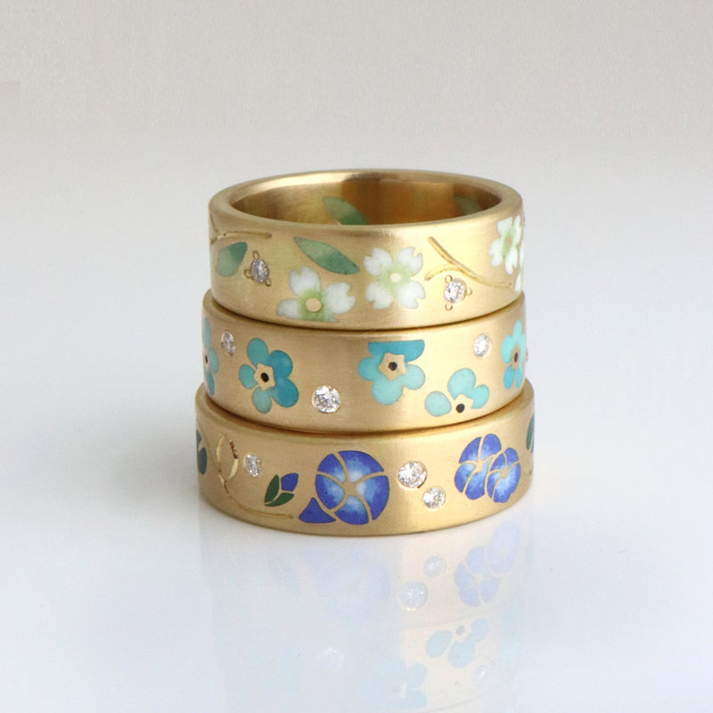 Three gold rings with ENAMEL floral patterns on a white background