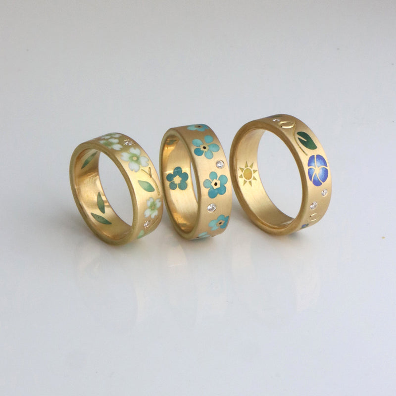 Three gold rings with ENAMEL floral designs on a light gray background