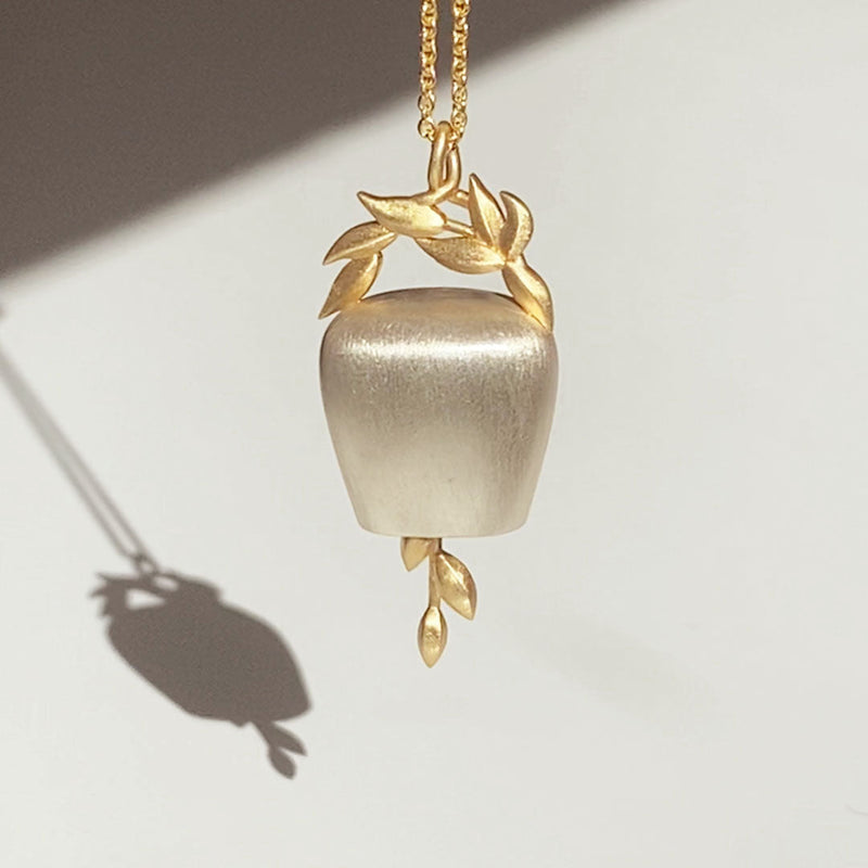 Gold and Silver Bell Pendant with Gold chain in sunlight with a shadow